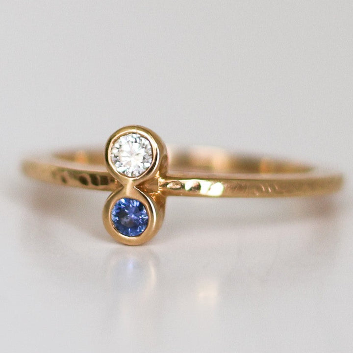 A stack of two rings, one with a round blue Montana Yogo Sapphire and the other with a round clear diamond, set in 14K gold with a hammered finish.