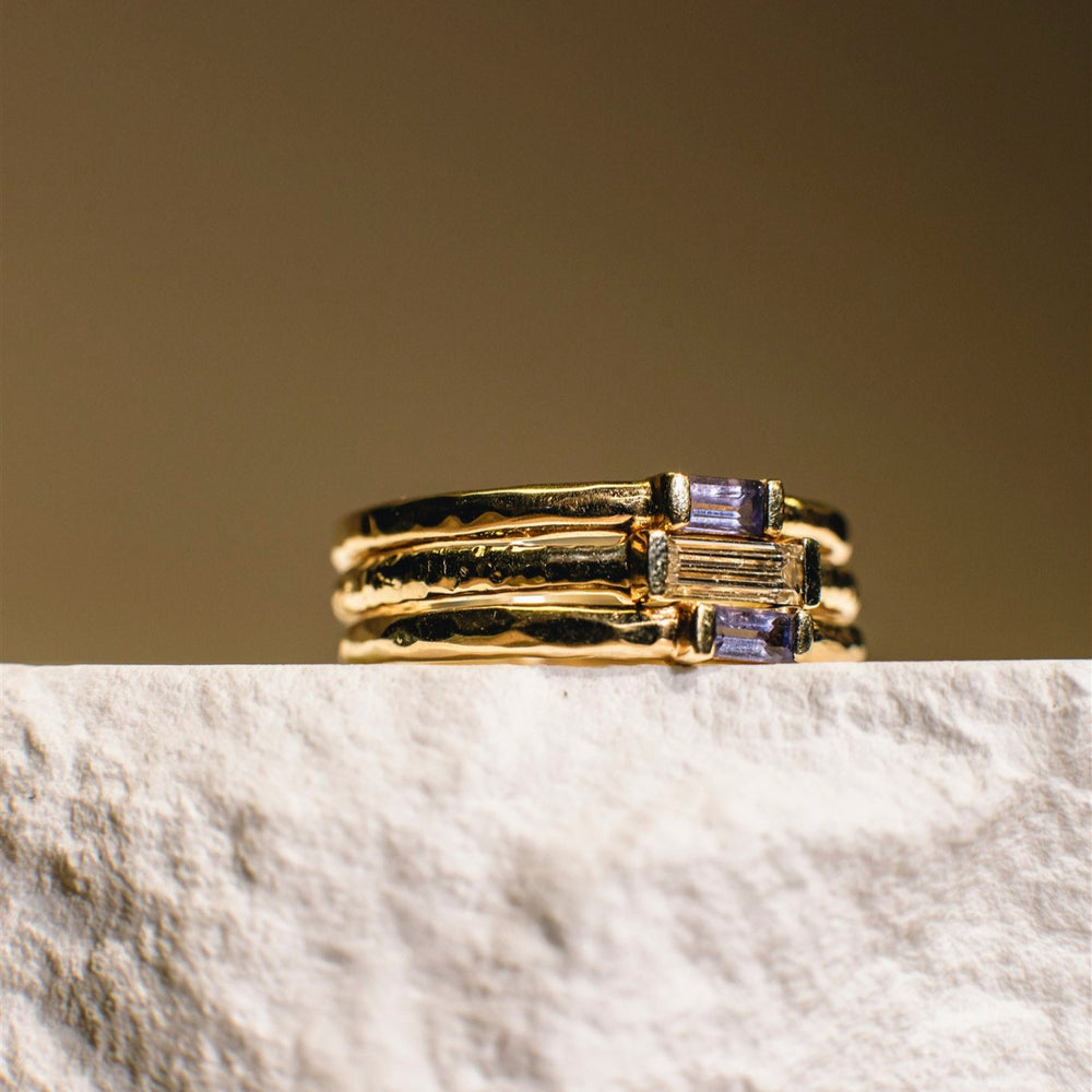 Gold ring with purple gemstones on a marble surface with a beige background