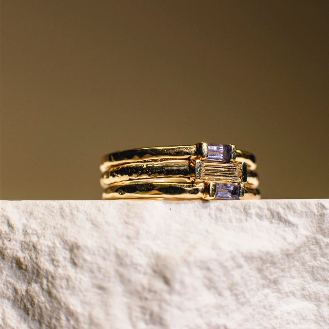 Gold ring with purple gemstones on a marble surface with a beige background