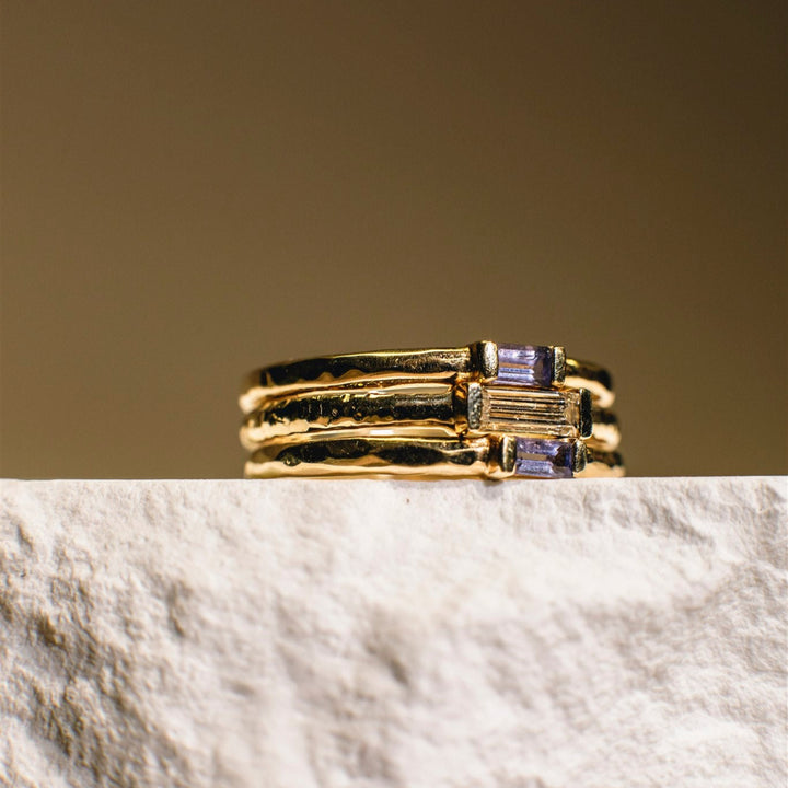 Gold ring with purple gemstones on a marble surface with a beige background