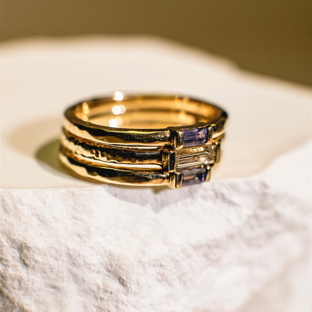 Gold ring with purple gemstones on a textured surface