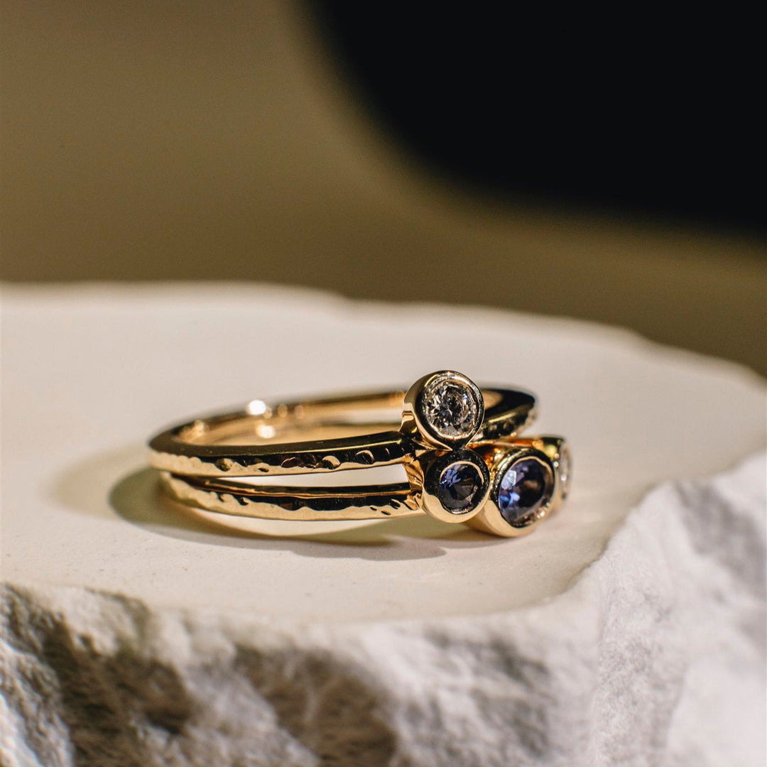 Two gold rings with gemstones on a textured surface