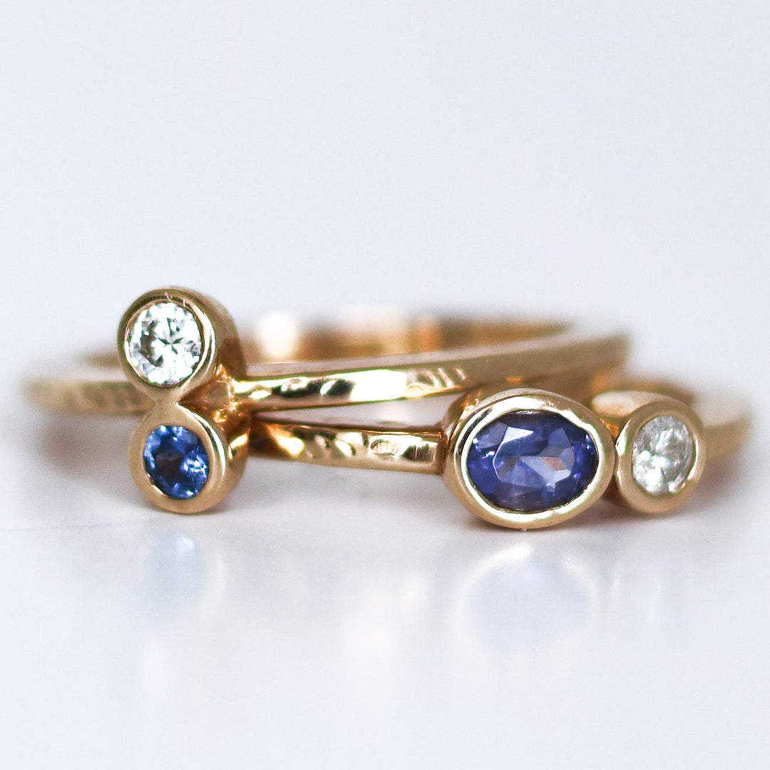 A stack of two rings, one with a round blue Montana Yogo Sapphire and the other with a round clear diamond, set in 14K gold with a hammered finish.