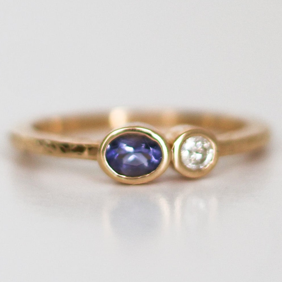 A stack of two rings, one with a round blue Montana Yogo Sapphire and the other with a round clear diamond, set in 14K gold with a hammered finish.
