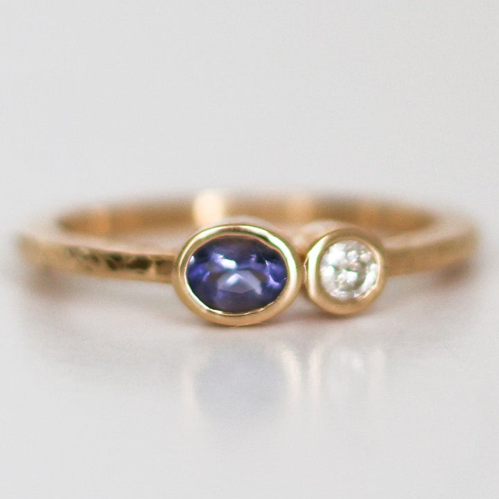 A stack of two rings, one with a round blue Montana Yogo Sapphire and the other with a round clear diamond, set in 14K gold with a hammered finish.