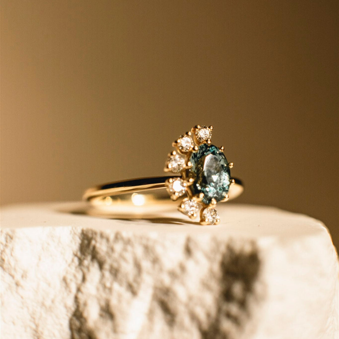 Gold ring with a central blue gemstone and smaller diamonds on a textured surface.