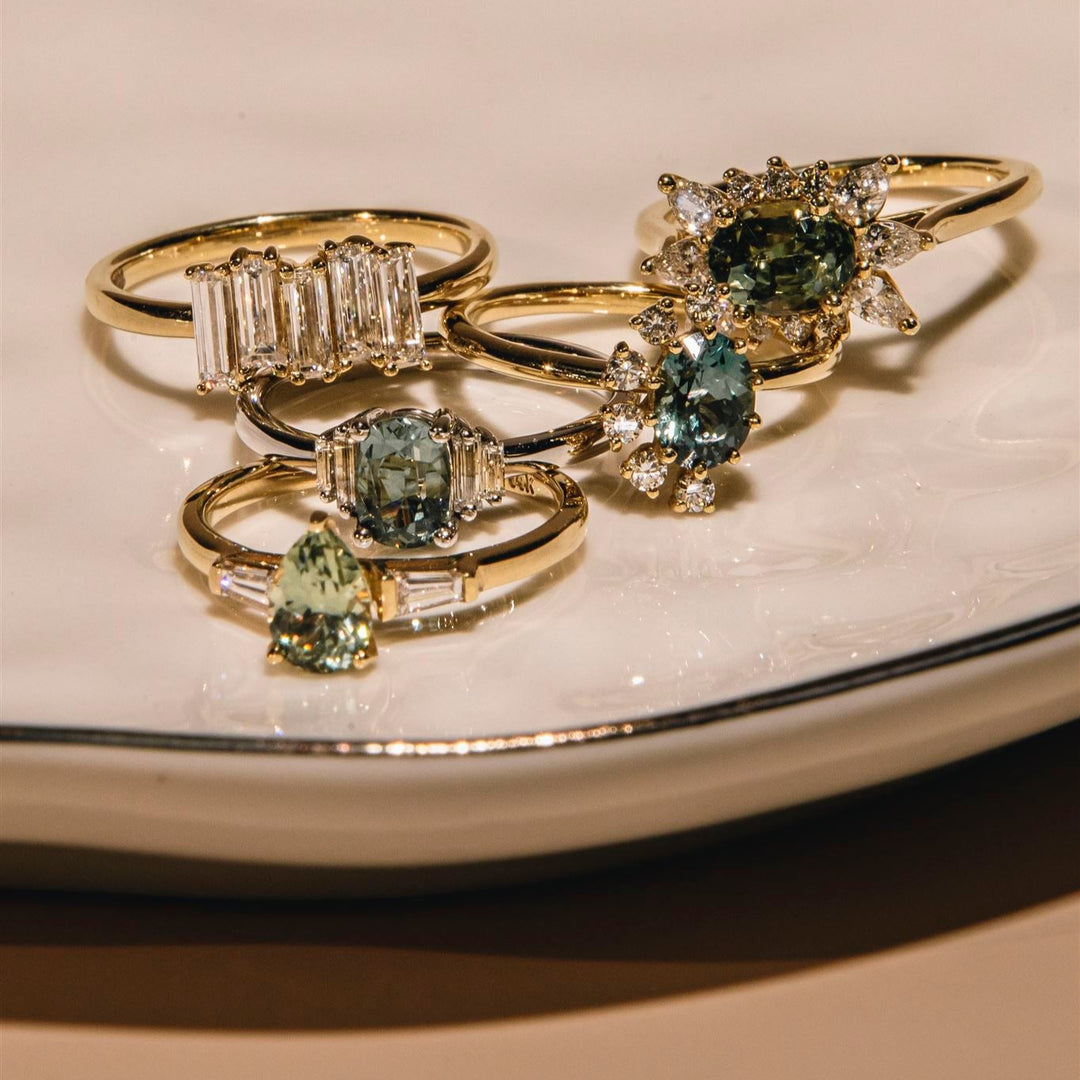 Set of gold rings with green gemstones on a beige surface