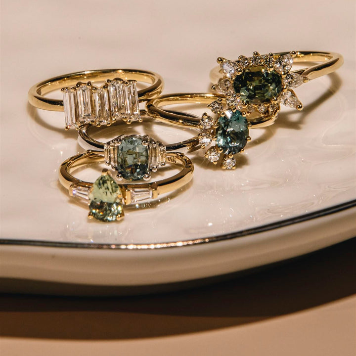 Set of gold rings with green gemstones on a beige surface