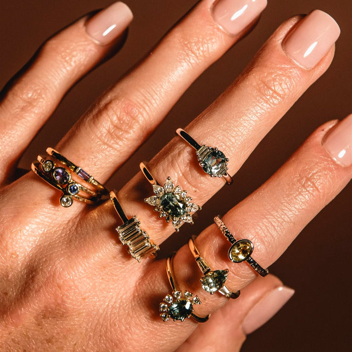 Hand wearing multiple rings with gemstones on a dark background