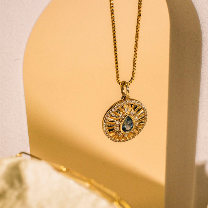 Gold necklace with a circular pendant on a beige arch