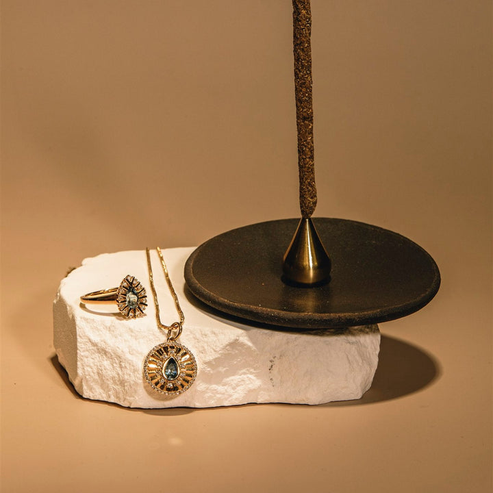 Jewelry stand with necklace and ring on a stone base against a beige background
