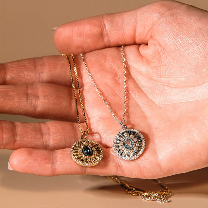 Hand holding two necklaces with pendants against a beige background