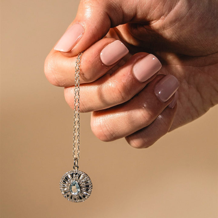 Hand holding a diamond pendant against a beige background