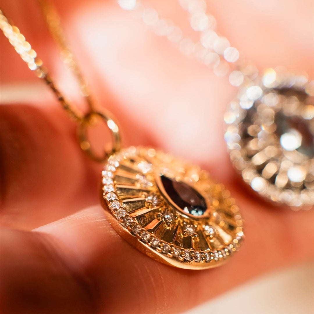 Gold pendant with a dark gemstone held between fingers against a blurred background