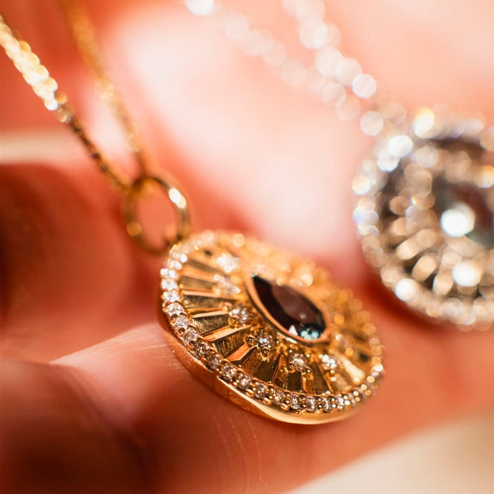 Gold pendant with a dark gemstone held between fingers against a blurred background