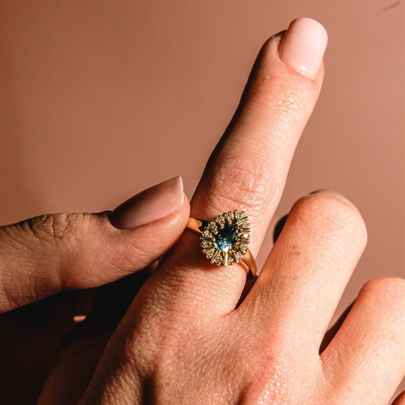 Close-up of a hand wearing a ring with a blue gemstone on a brown background