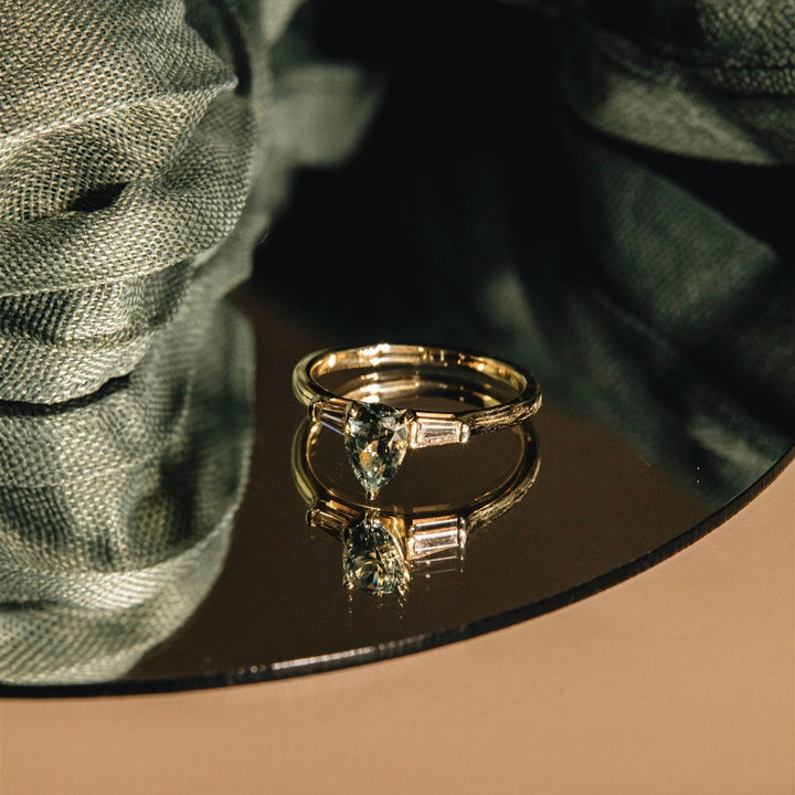 Gold ring with a diamond on a reflective surface with green fabric in the background