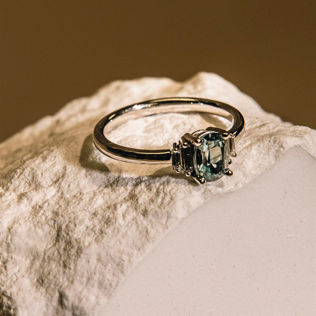 White gold ring with a green gemstone on a textured surface