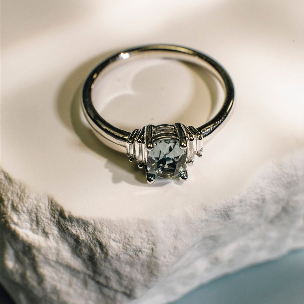 White gold ring with a central gemstone on a marble surface