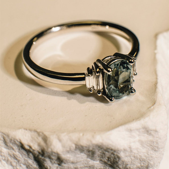 Silver ring with a large central gemstone and smaller side stones on a textured surface