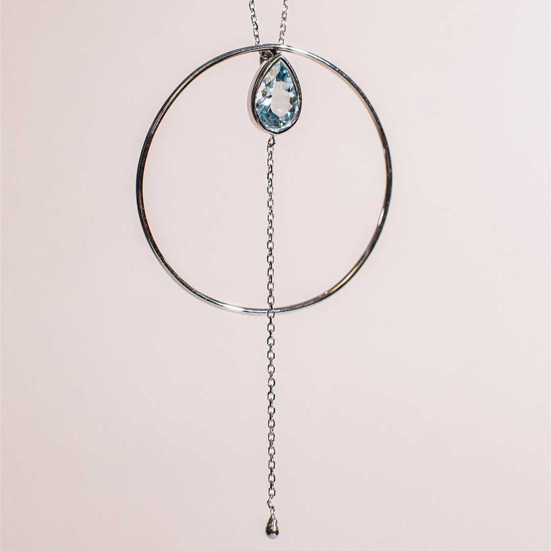 Necklace with a circular pendant and teardrop-shaped gemstone on a light background