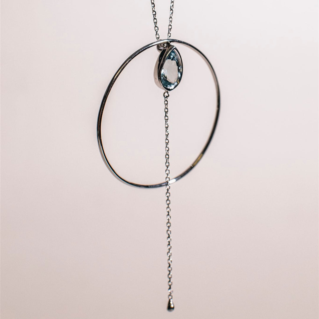 Necklace with circular pendant and chain on a light pink background