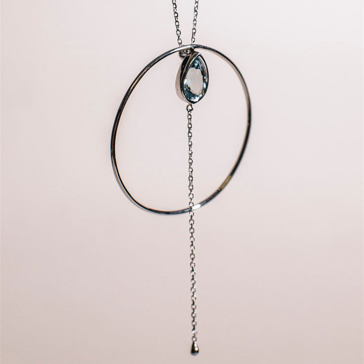 Necklace with circular pendant and chain on a light pink background