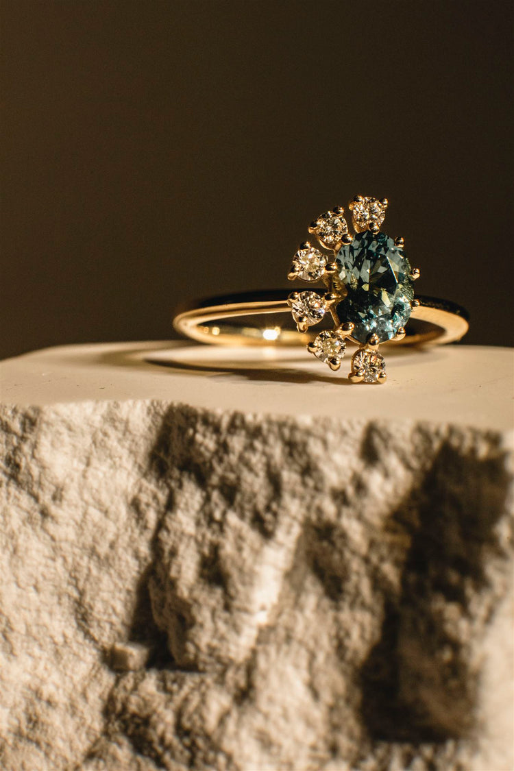 A Montana sapphire halo ring in 14K gold resting on rough carved stone