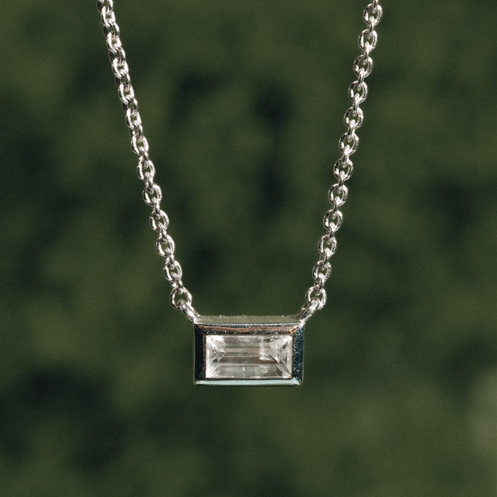 Silver necklace with a rectangular gemstone pendant against a blurred green background