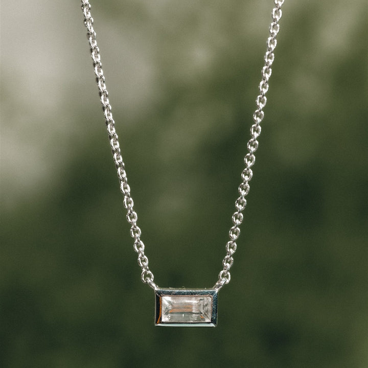 Silver necklace with a rectangular pendant against a blurred green background