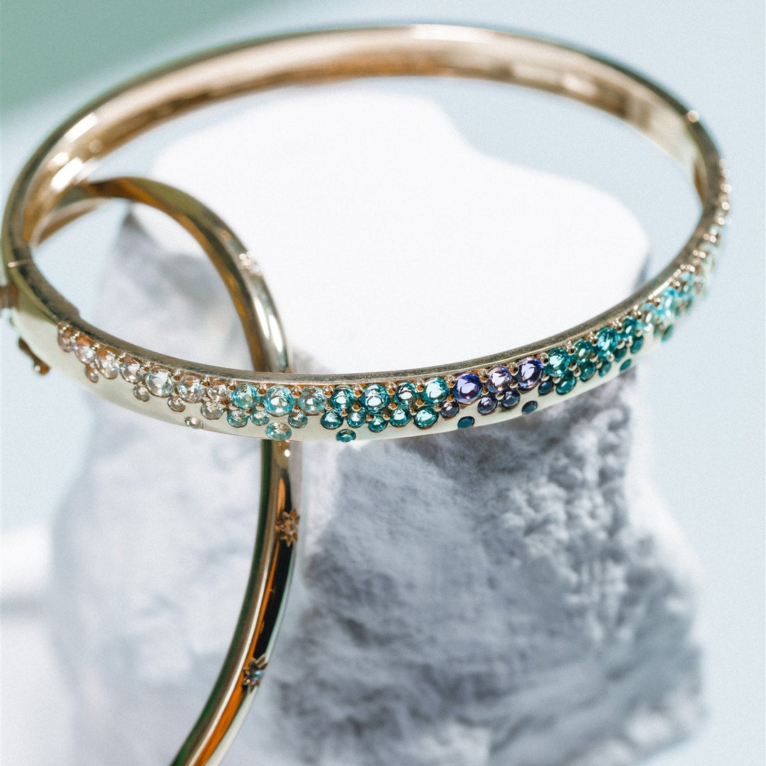 Gold bangles with gemstone accents on a marble surface