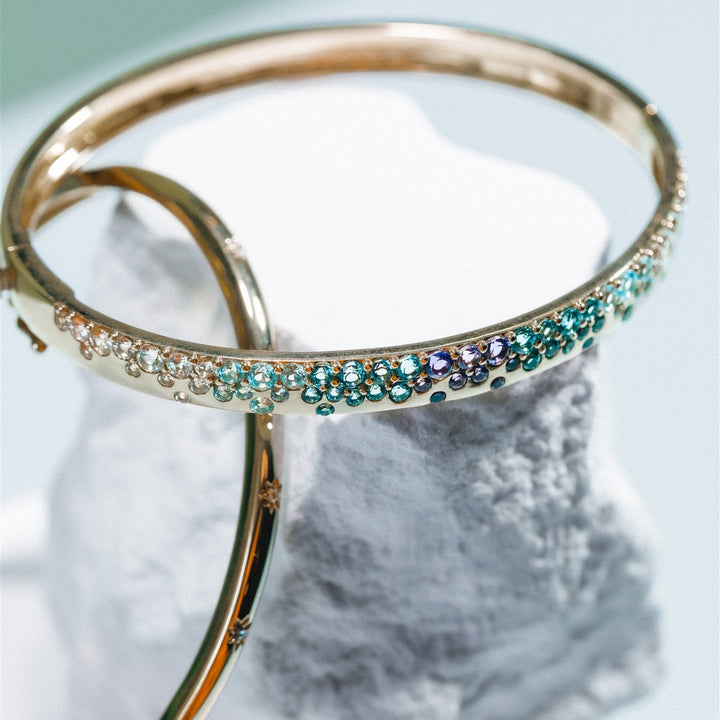 Gold bangles with gemstone accents on a marble surface
