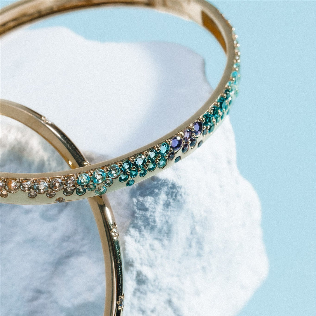 Gold bangles with gemstones on a white shell against a light blue background
