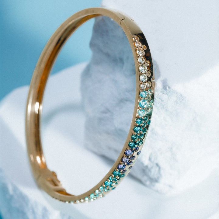 Gold bracelet with gemstones on a white shell against a light blue background