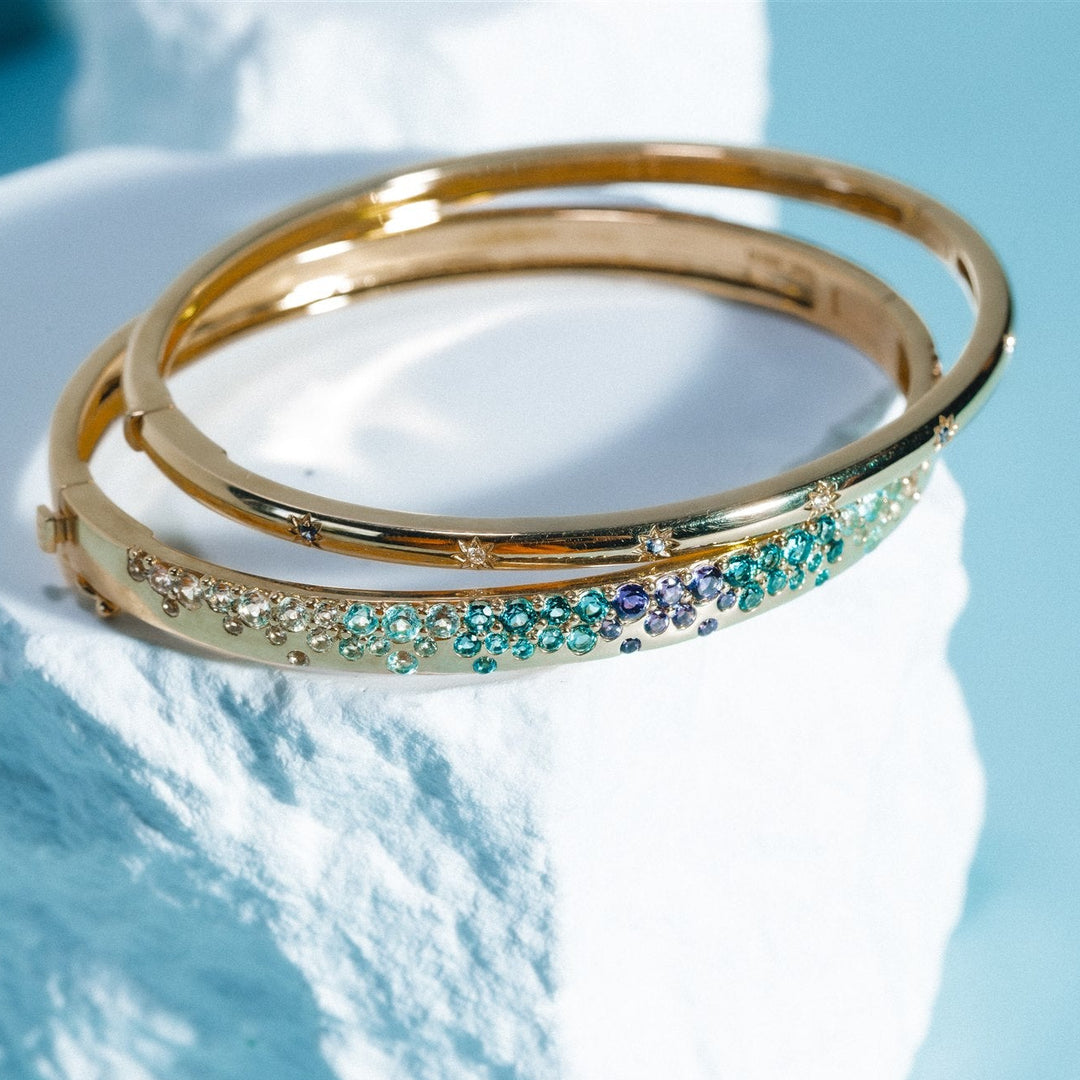 Gold bangle with gemstones on a white block against a light blue background