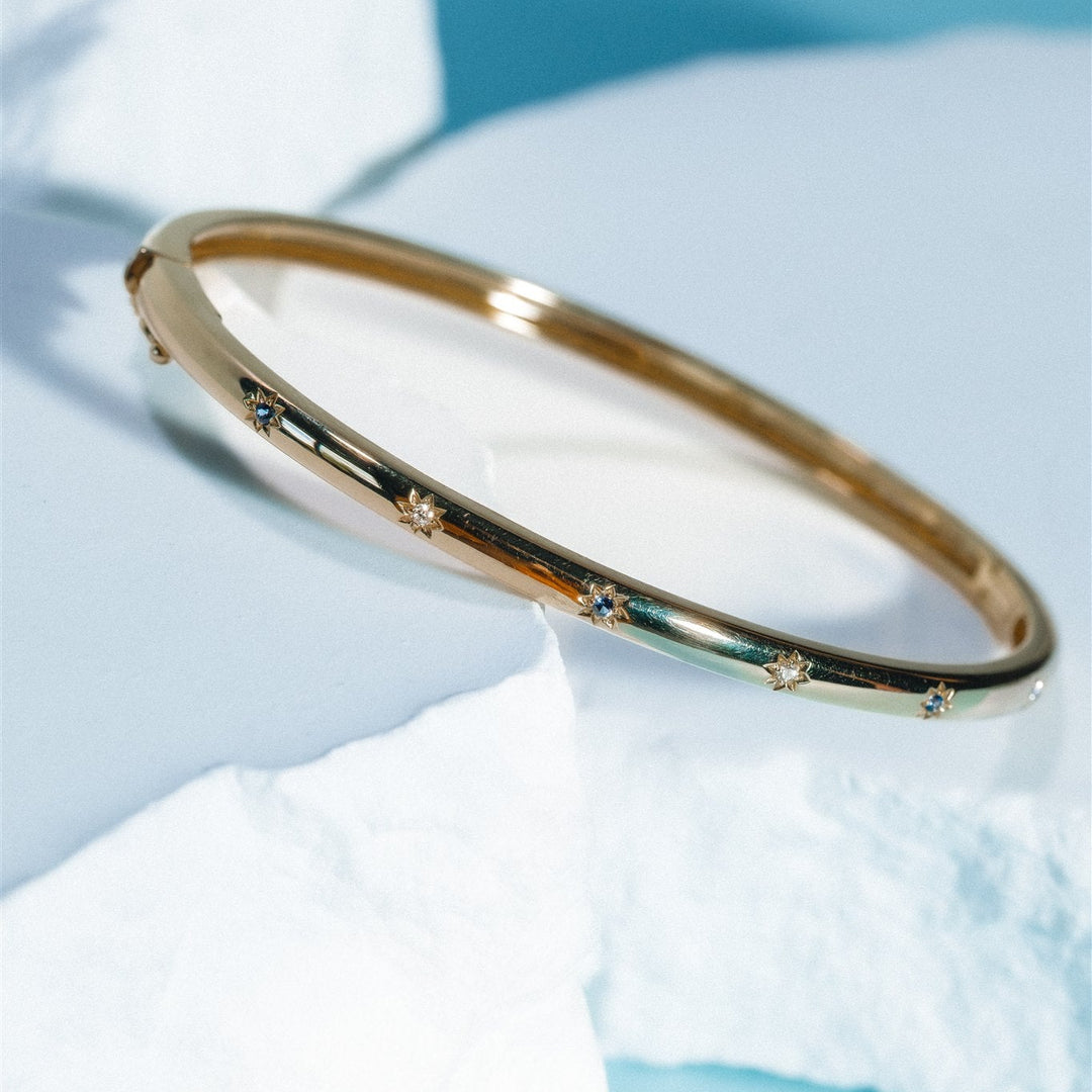 Gold bracelet with small stones on a white shell against a blue background