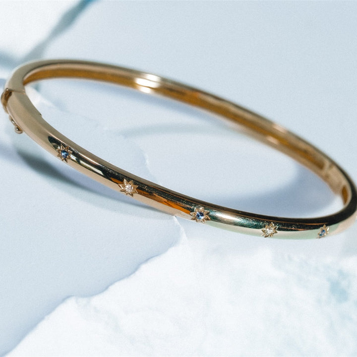 Gold bracelet with small diamonds on a light blue background