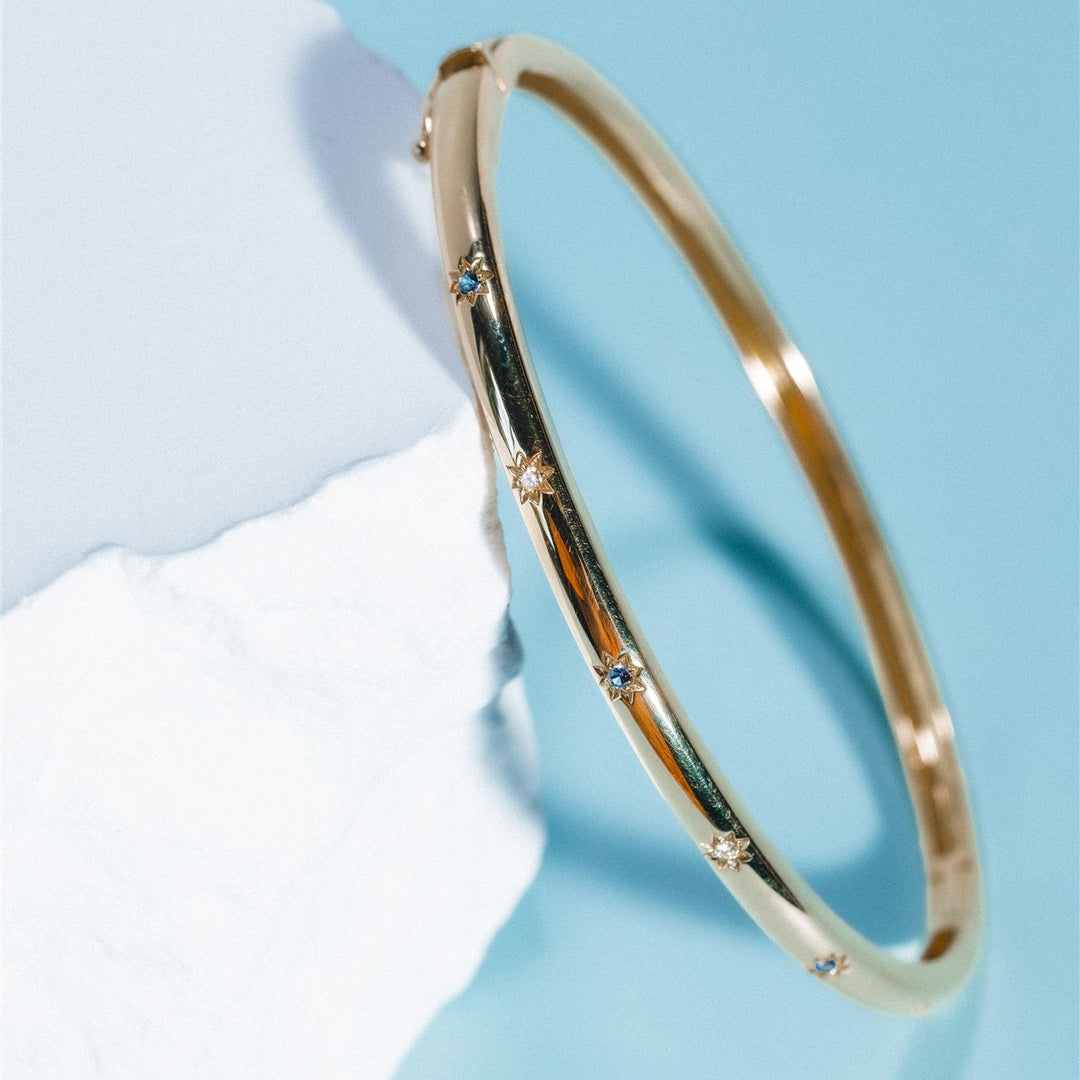 Gold bangle with small stones on a light blue background