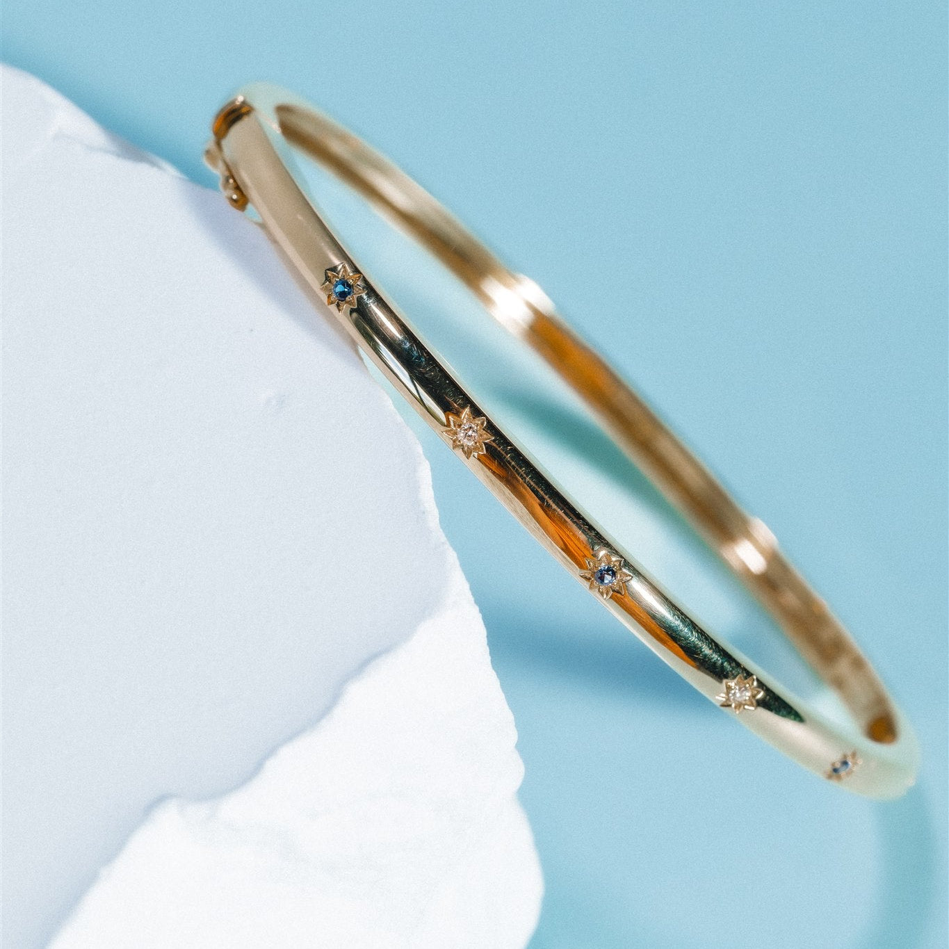 Gold bracelet with blue gemstones on a light blue background