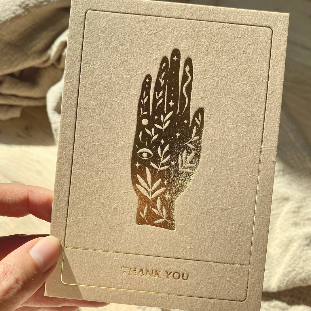 Beige card with palmistry design and 'THANK YOU' text held by a hand.