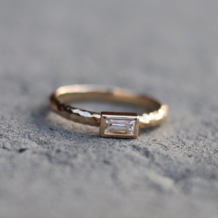 Gold ring with a white sapphire on a textured gray surface