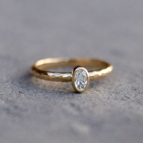 Gold ring with a white sapphire on a textured gray surface