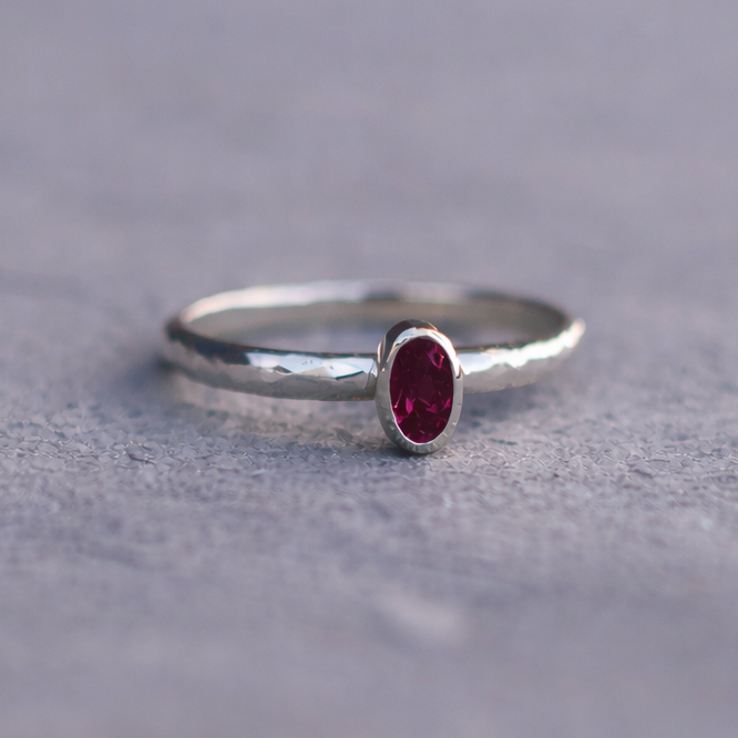 Silver ring with a red gemstone on a gray surface