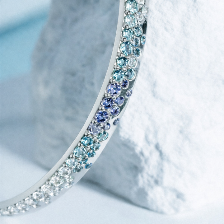 Close-up of a silver bangle with multicolored stones on a textured white surface.