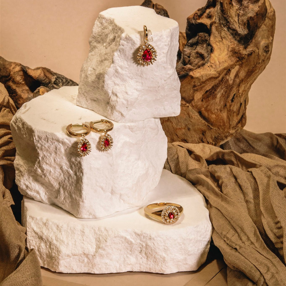 Jewelry set including earrings and a ring displayed on a textured white surface with a natural wood background.