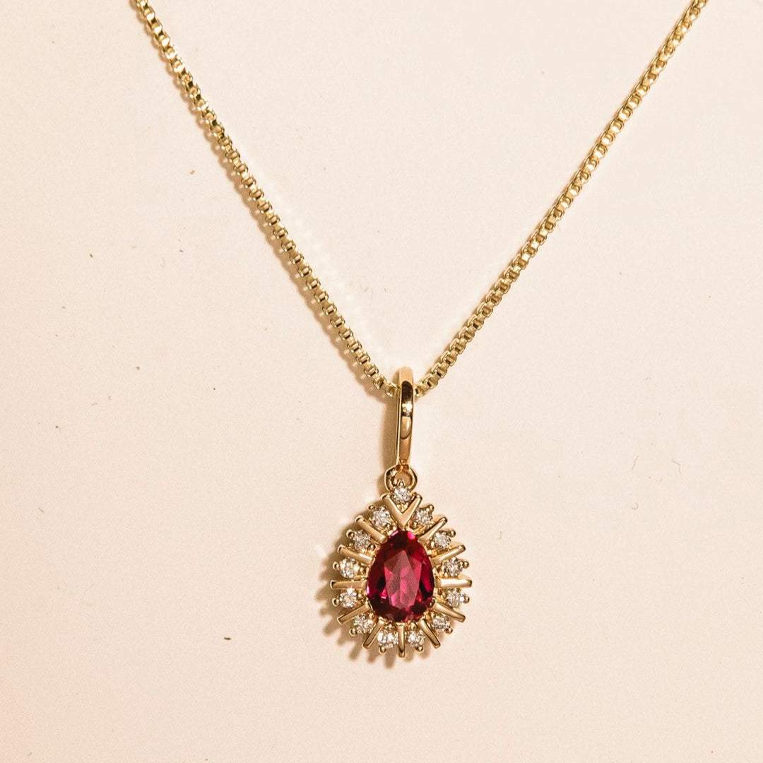 Gold necklace with a red gemstone pendant on a beige background