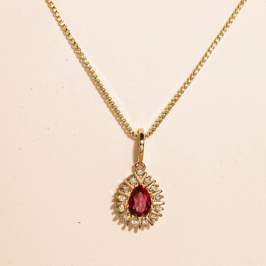 Gold necklace with a red gemstone pendant on a beige background
